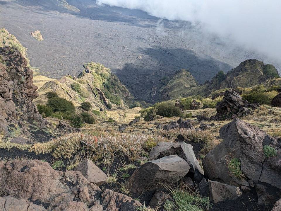 Rocce laviche ed erba alla Schiena dell'Asino, con la Valle del Bove sotto le nuvole