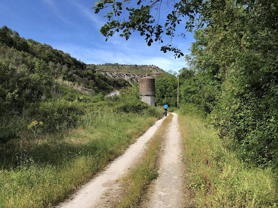 La carrareccia dell'ex ferrovia nella valle, con una vecchia torre dell'acqua sullo sfondo